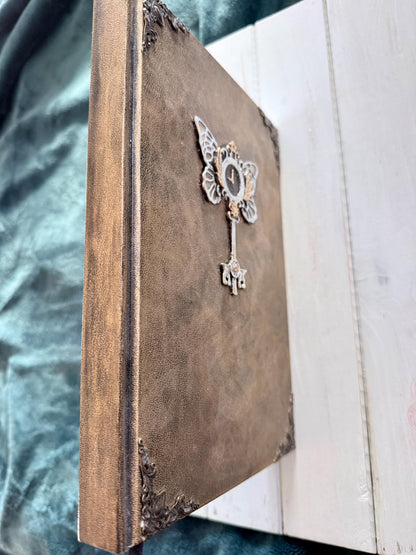 A decorative Heart Key embellishment is coated in clear resin on a hardcover journal measuring 10”x7.5”x1”