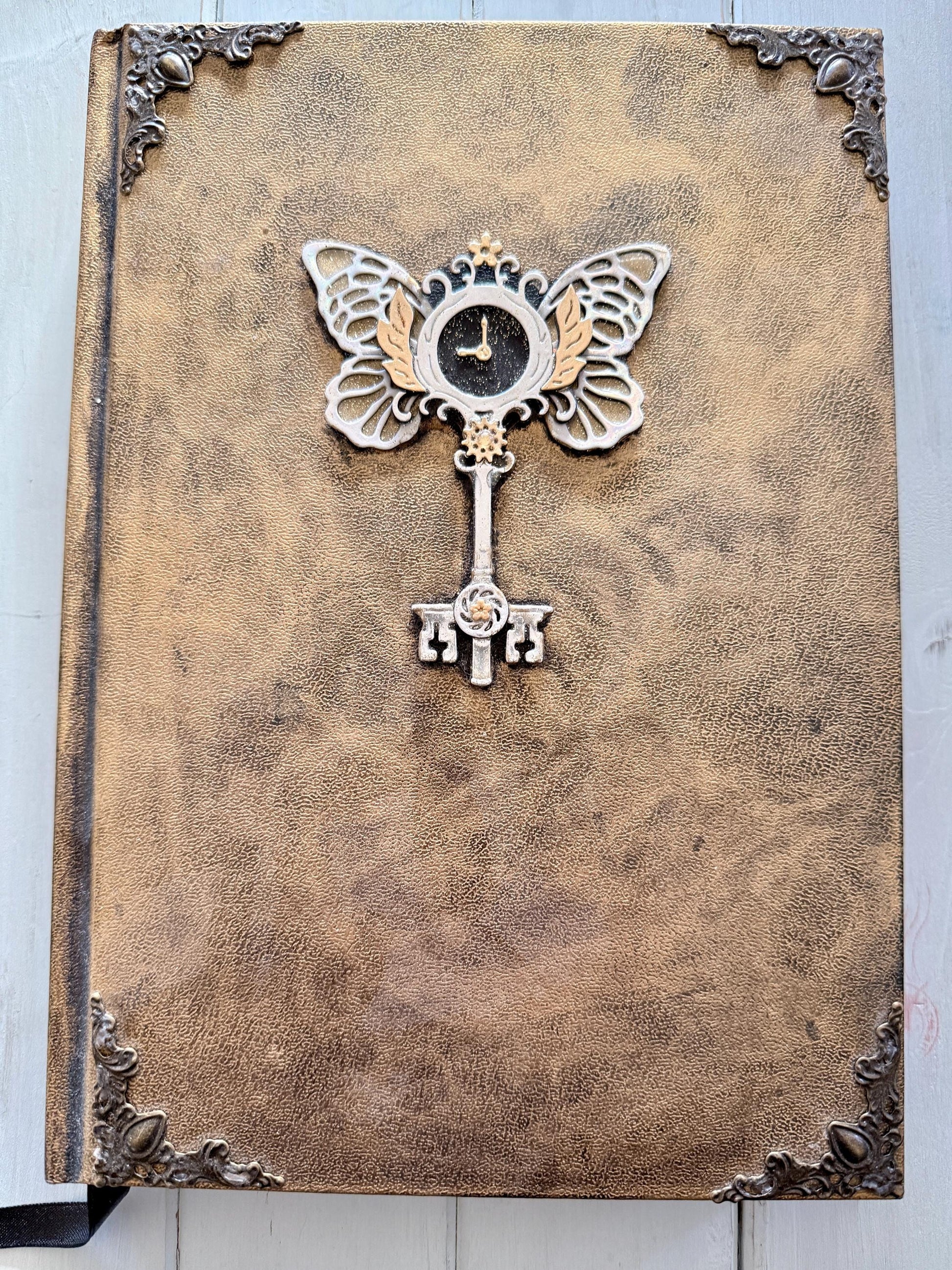 A decorative Heart Key embellishment is coated in clear resin on a hardcover journal measuring 10”x7.5”x1”