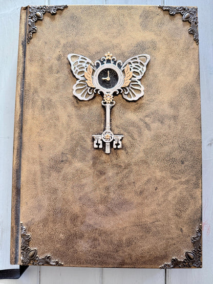 A decorative Heart Key embellishment is coated in clear resin on a hardcover journal measuring 10”x7.5”x1”