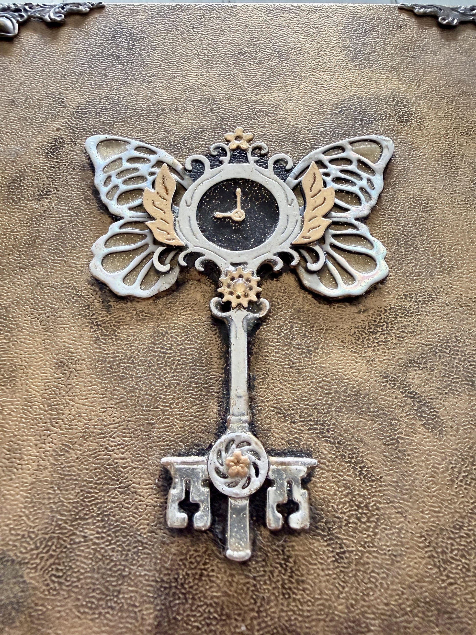 A decorative Heart Key embellishment is coated in clear resin on a hardcover journal measuring 10”x7.5”x1”